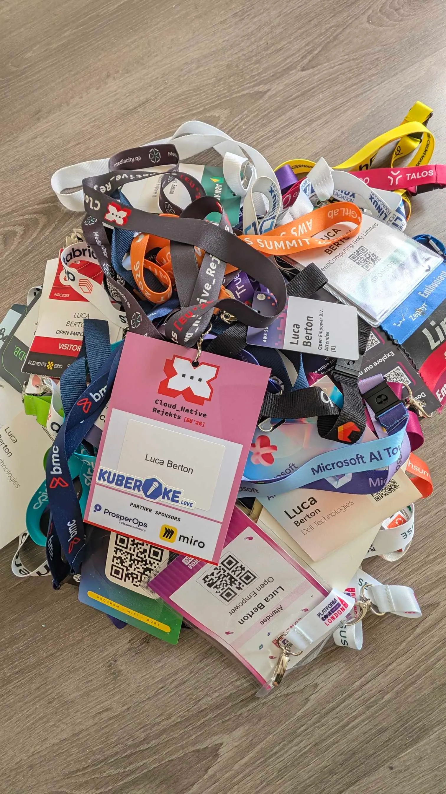 Conference badges and lanyards piled on a floor, including Cloud_Native Rejekts EU '26