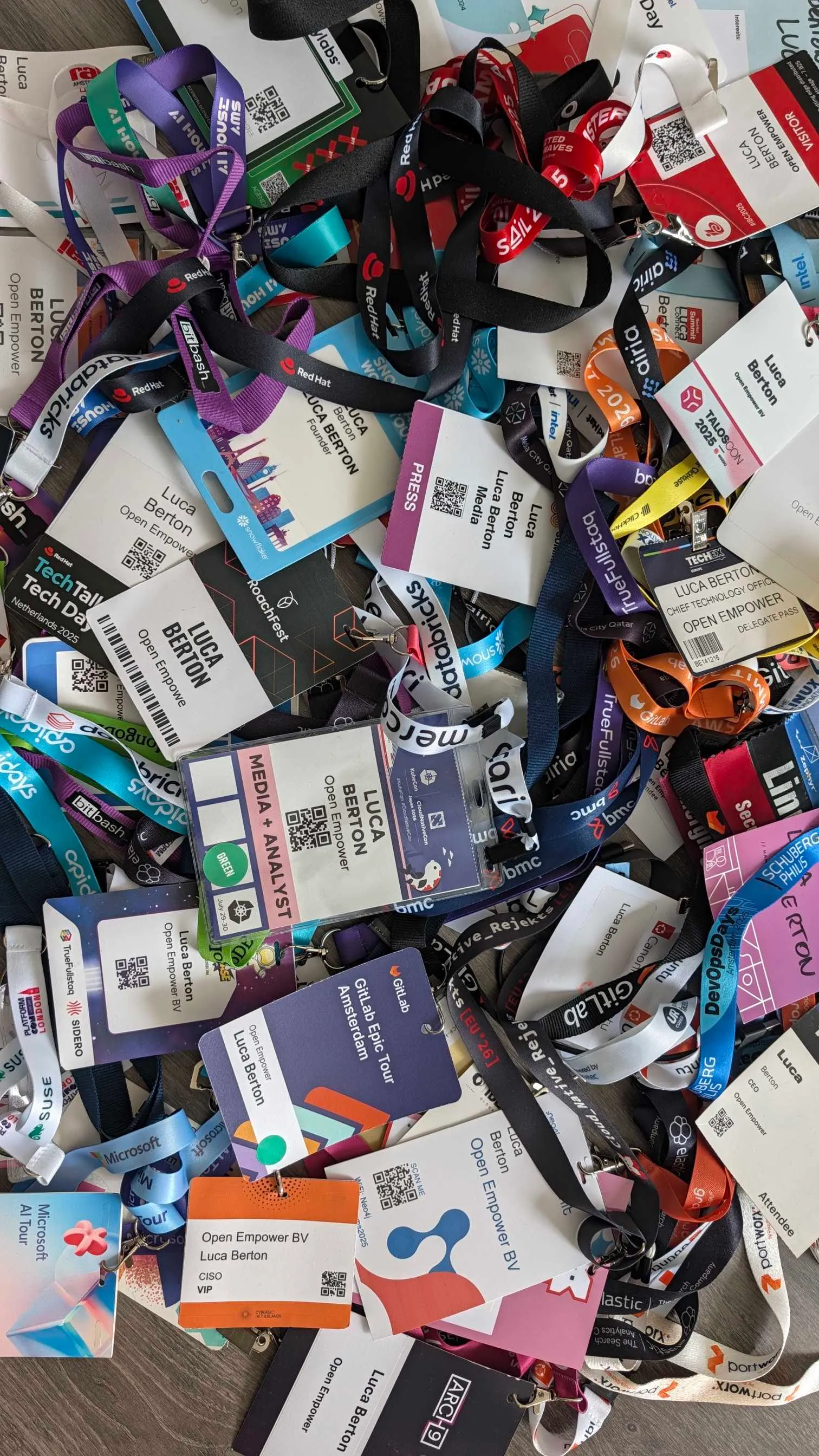 A dense pile of tech conference badges for Luca Berton
