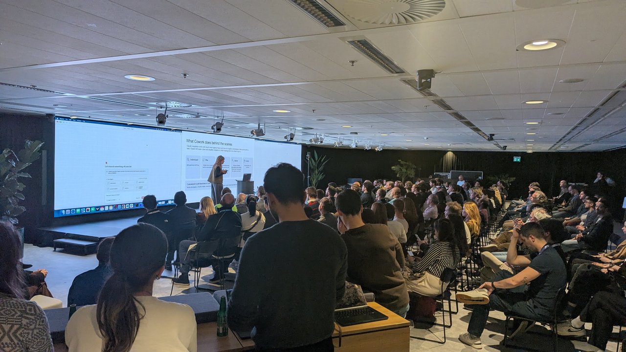 Speaker presenting the What Cowork does behind the scenes slide next to the Claude desktop app at AI House Amsterdam