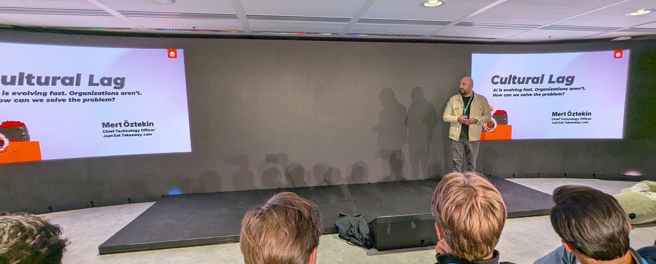 Mert Ăztekin on the AI House stage next to his title slide Cultural Lag: AI is evolving fast. Organizations aren't. How can we solve the problem? naming him Chief Technology Officer, Just Eat Takeaway.com