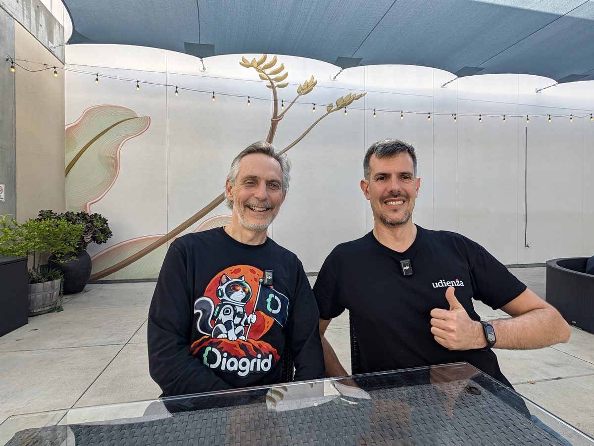 Mark Fussell, in a black Diagrid sweatshirt, and Luca Berton giving a thumbs-up at a table in the San Jose convention center