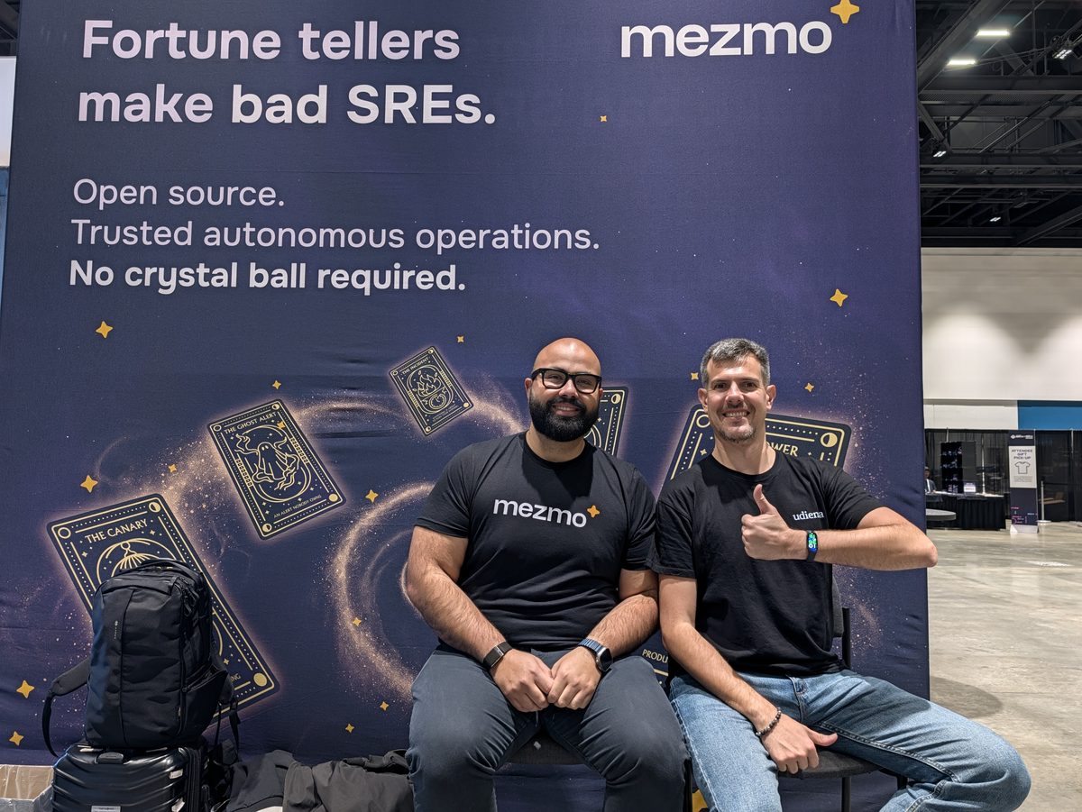 Andre Elizondo and Luca Berton in front of the Mezmo booth wall that reads Fortune tellers make bad SREs
