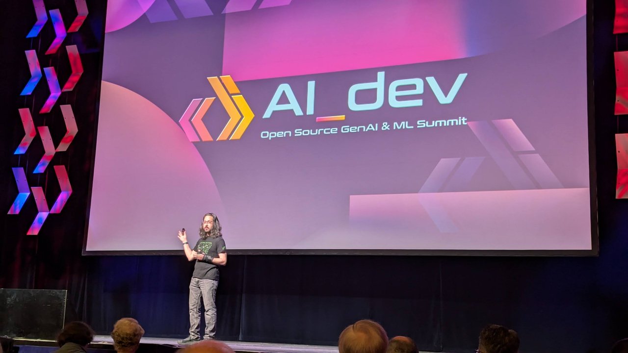 The AI_dev Open Source GenAI and ML Summit title slide on the main stage at RAI Amsterdam, with the host on stage