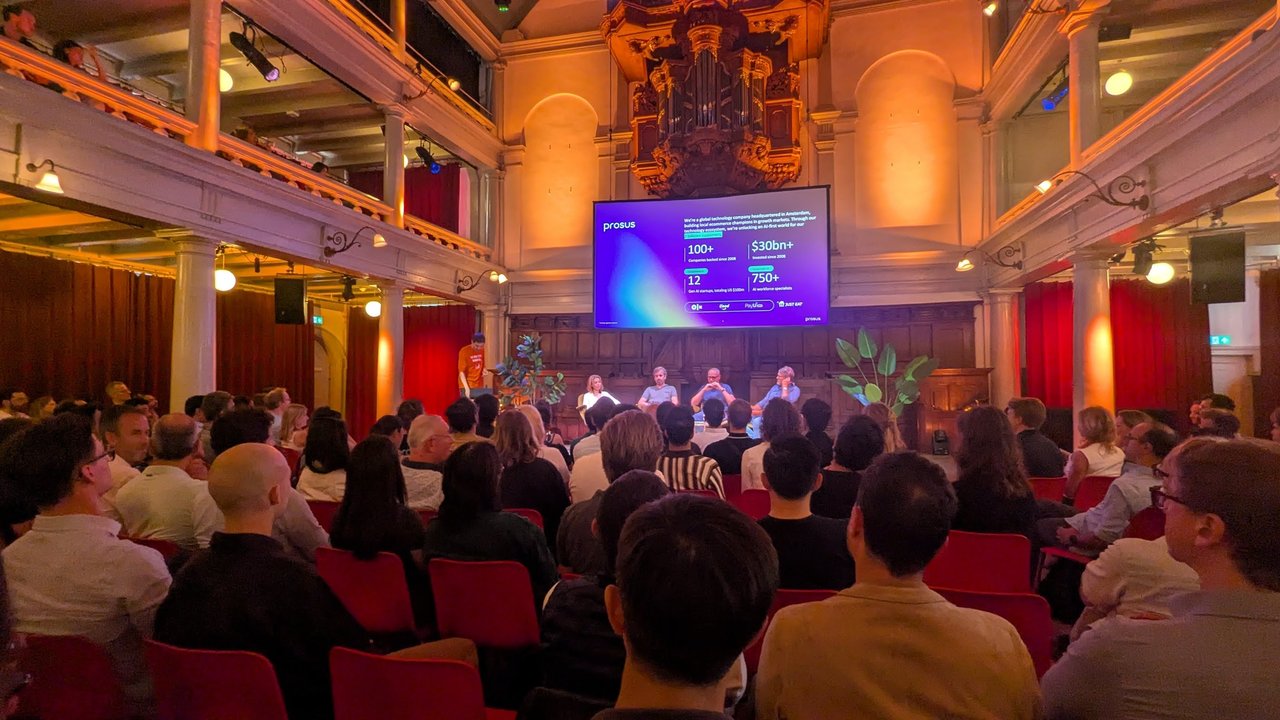Wide view of a full hall with the Prosus slide on screen and four panellists seated at the front