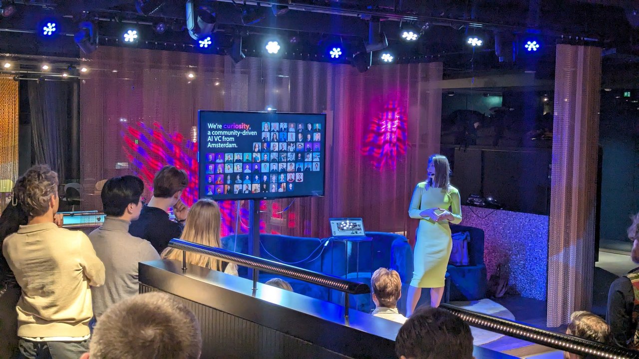 Speaker at AI Salon Amsterdam presenting the slide We're curiosity, a community-driven AI VC from Amsterdam, with a grid of community member photos