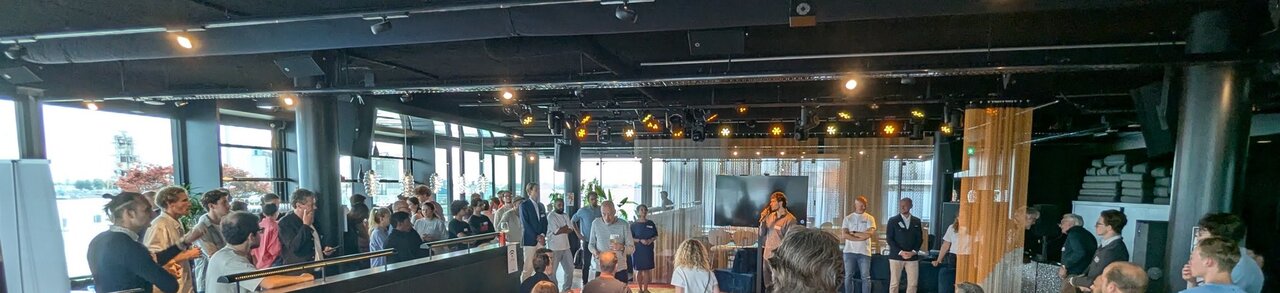 The room during the talks at AI Salon Amsterdam, with a speaker standing at the front and a standing crowd around the stage
