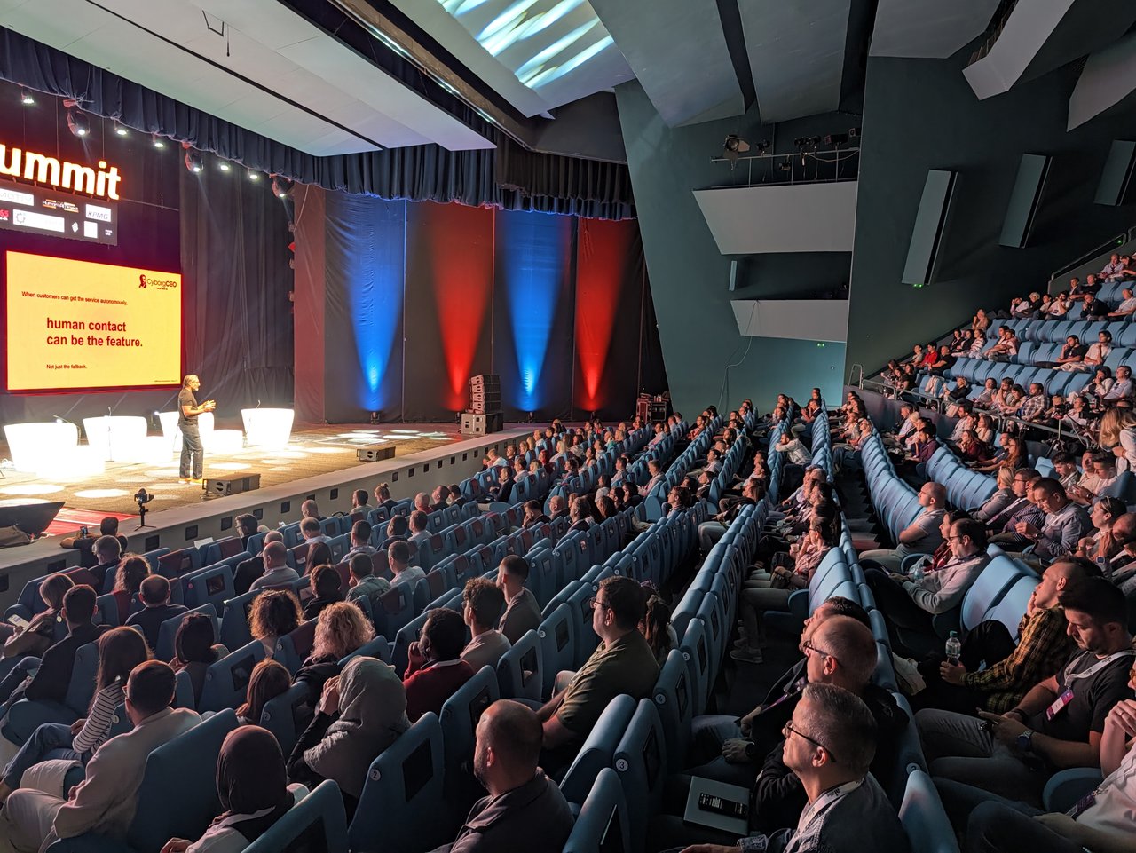 A packed opera auditorium watching a speaker on the Main Stage next to a slide reading human contact can be the feature