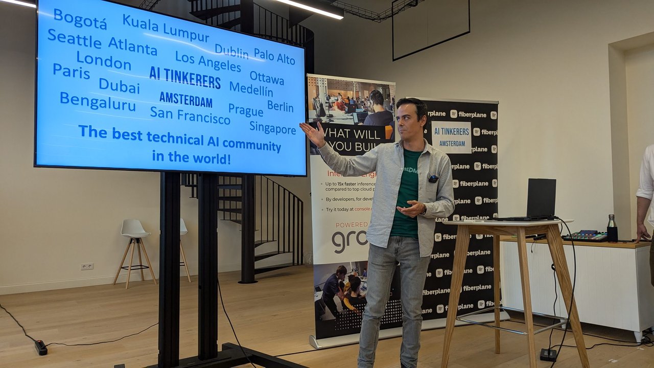 The host in front of a word cloud of AI Tinkerers cities around Amsterdam, titled the best technical AI community in the world