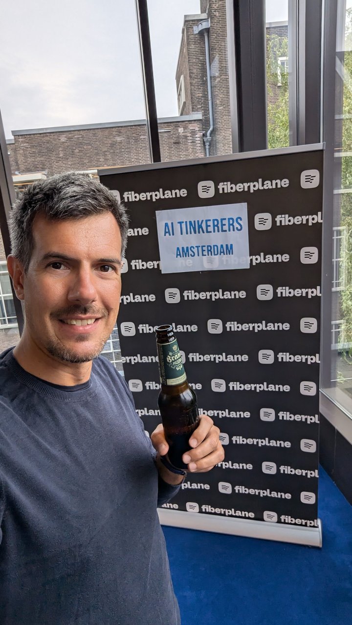 Luca Berton holding a beer in front of the Fiberplane step-and-repeat wall with an AI Tinkerers Amsterdam sign