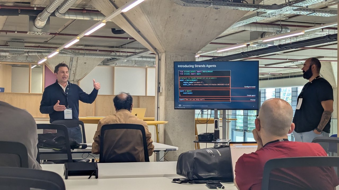 A presenter in front of the Introducing Strands Agents slide showing Python code that imports BedrockModel and Agent, configures a Claude 3.5 Haiku model in us-east-1 and prompts the agent
