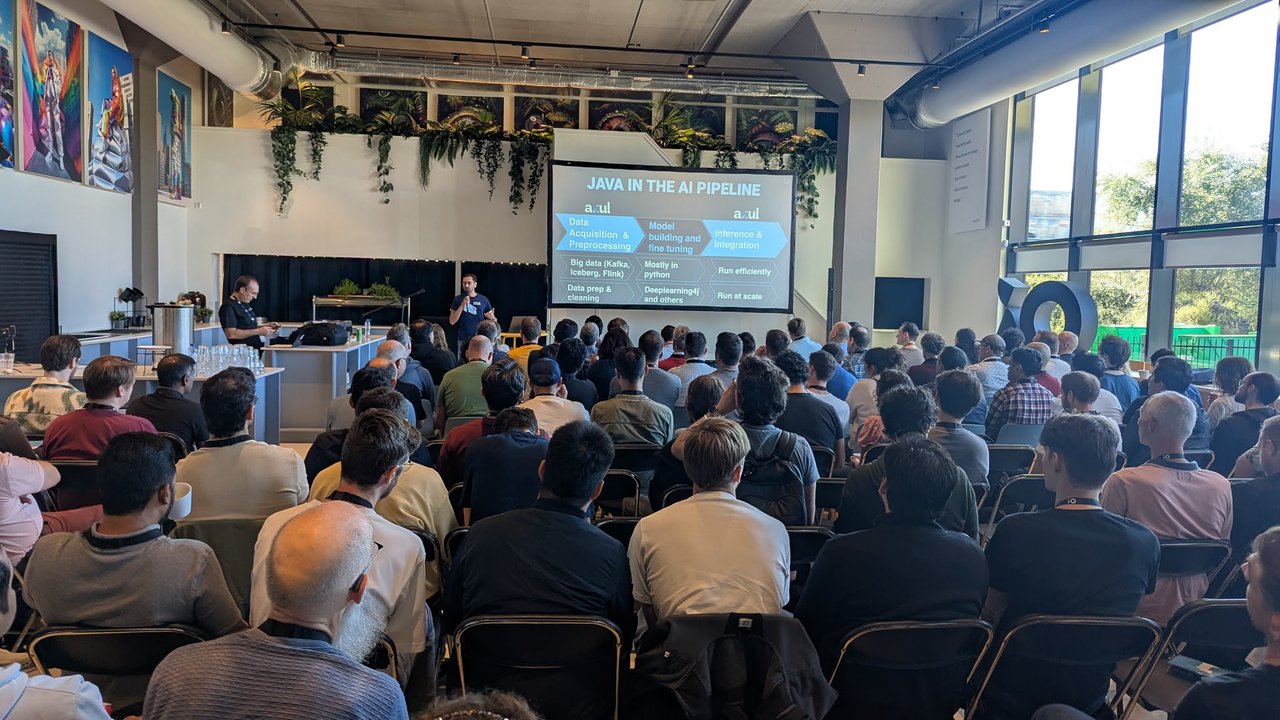 Pratik Patel on stage in a full room at iO Campus, with the slide Java in the AI pipeline showing data acquisition, model building and inference stages