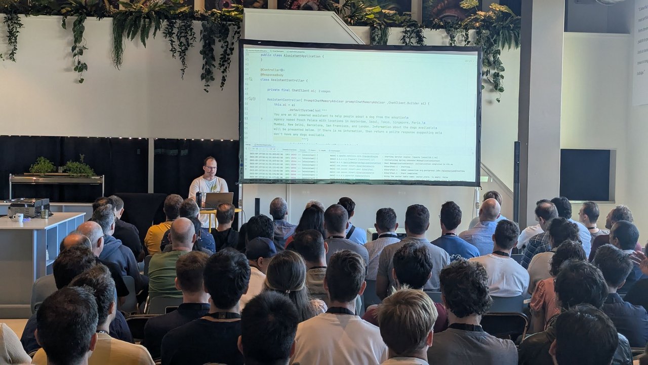 Josh Long live coding at the lectern in front of a projected AssistantController class in Spring AI, with the Pooch Palace dog adoption system prompt and a PromptChatMemoryAdvisor in the constructor