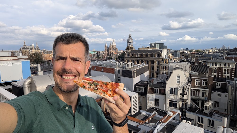 Luca holding a slice of pizza on the StartDock rooftop terrace