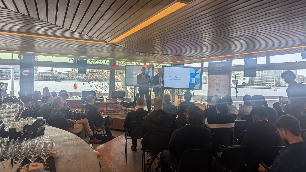The Full MCP Lifecycle workshop at Apidays Amsterdam 2025, with two presenters at a lectern and the river IJ through the windows behind them