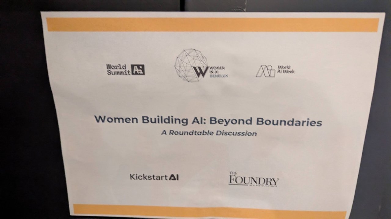 Printed sign reading Women Building AI: Beyond Boundaries, A Roundtable Discussion, with World Summit AI, Women in AI Benelux, World AI Week, Kickstart AI and The Foundry logos