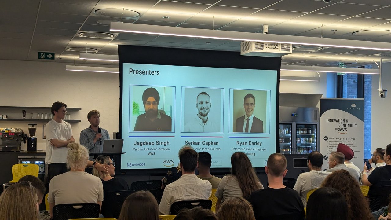 Datadog User Group GenAI Meetup presenters slide listing Jagdeep Singh of AWS, Serkan Capkan and Ryan Earley of Datadog, with the hosts at the side of the stage