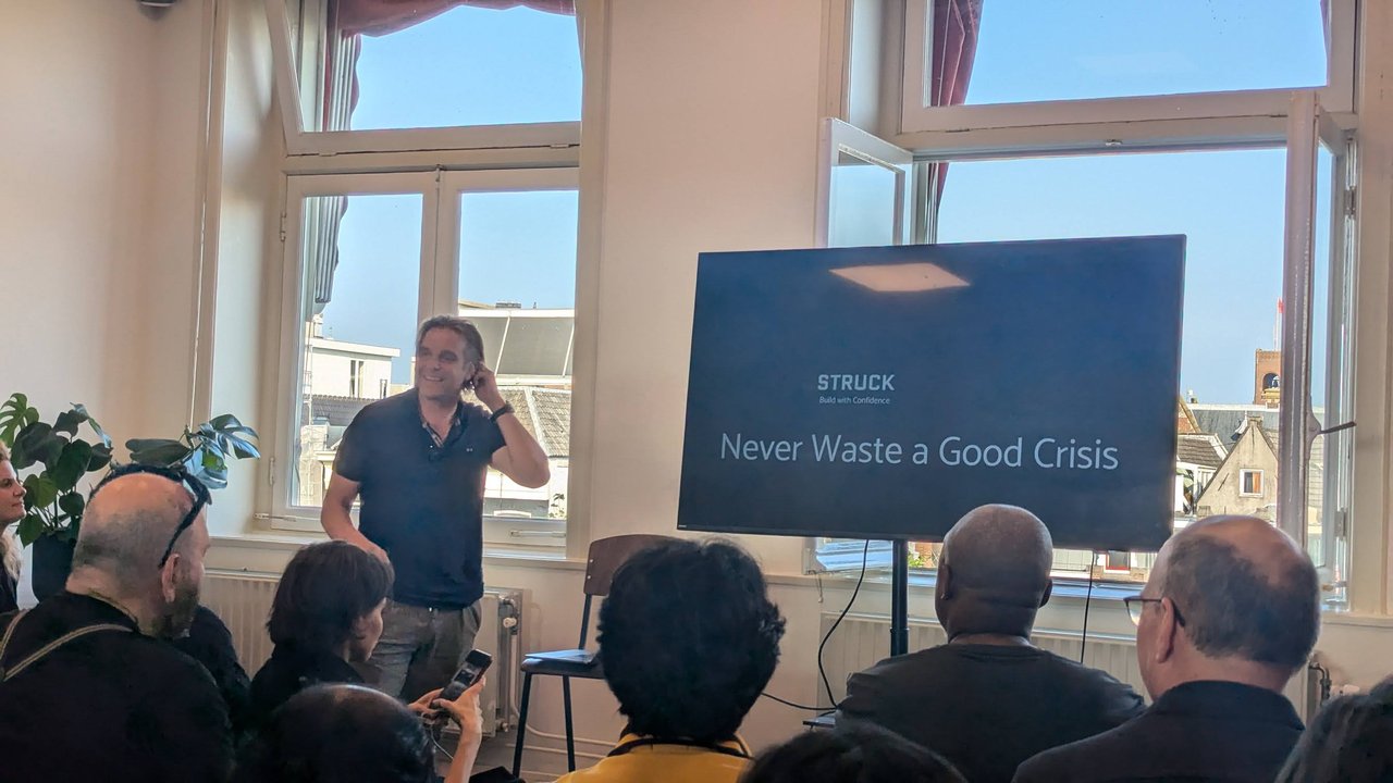 STRUCK speaker in front of the "Never Waste a Good Crisis" title slide with the STRUCK "Build with Confidence" logo