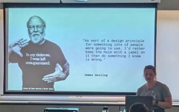 A speaker at the Amsterdam JUG standing next to a slide with a quote attributed to James Gosling about keeping a hole with a label on it