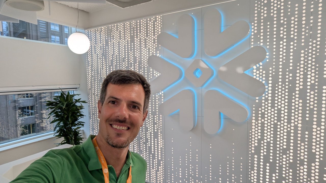 Selfie of Luca in front of a backlit Snowflake logo wall at the Snowflake Experience Centre in Amsterdam