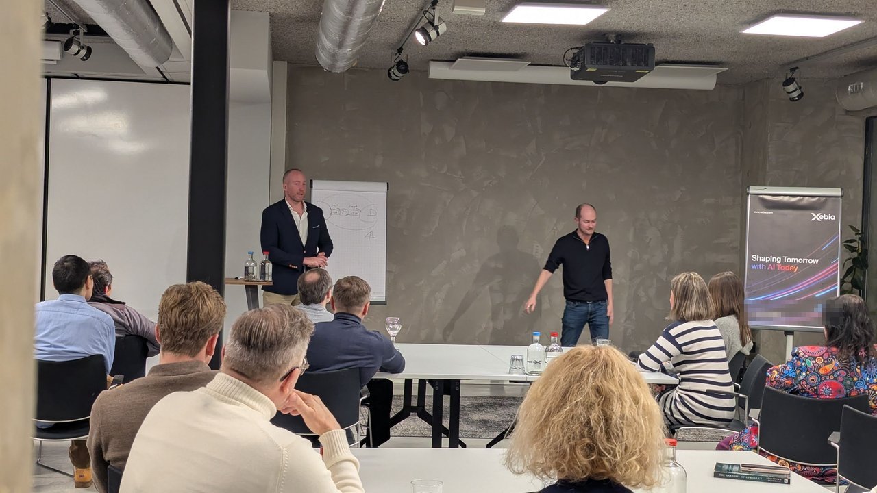Two speakers presenting at a flip chart in a Xebia meeting room, with a Shaping Tomorrow with AI Today banner on the right