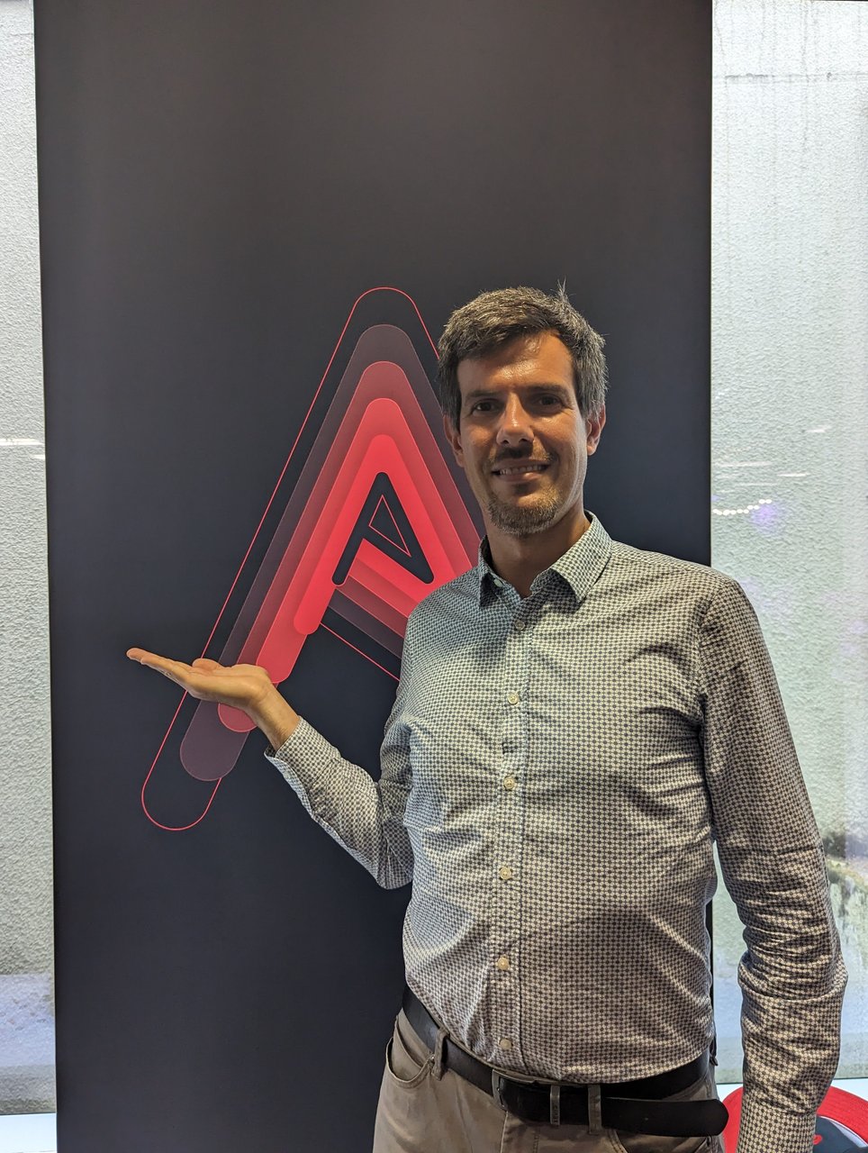 Luca Berton standing next to a tall dark banner with the red layered Ansible A logo at CodeNode