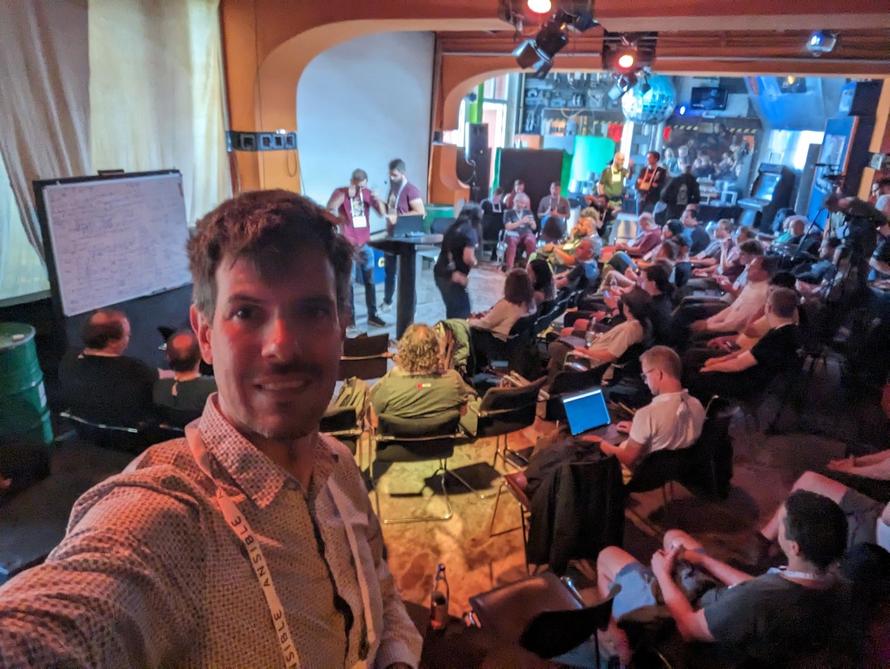 Luca Berton taking a selfie in the packed main hall at c-base during Ansible Community Day Berlin 2023