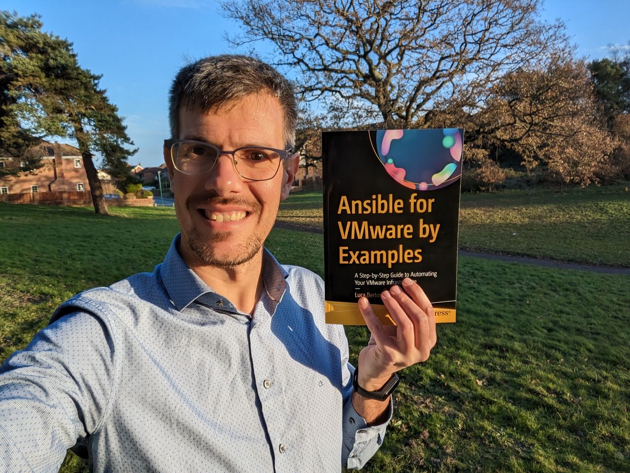 Luca Berton outdoors holding a printed copy of his book Ansible for VMware by Examples