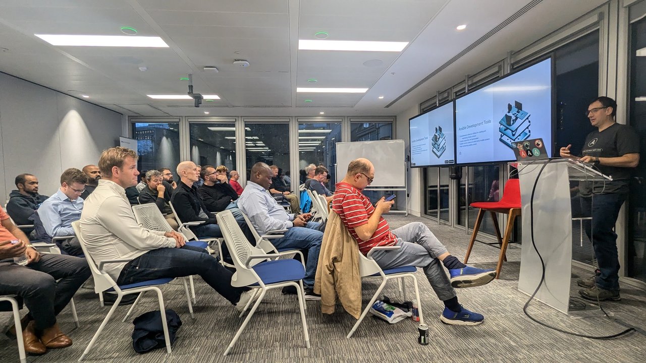 The audience in the Dell Technologies meeting room in London listening to the Ansible Development Tools talk, with slides on two screens