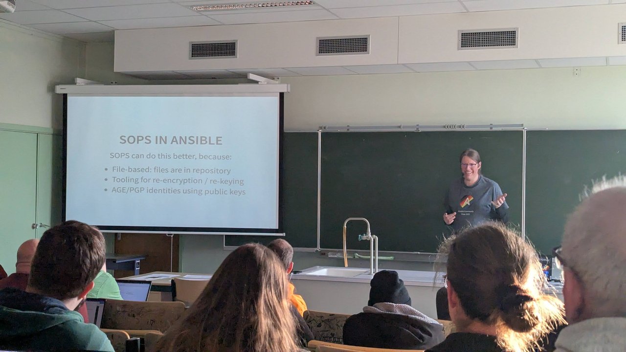 A "SOPS in Ansible" slide at CfgMgmtCamp 2025 in Ghent saying SOPS can do this better because it is file-based, has tooling for re-encryption and re-keying, and uses AGE/PGP identities with public keys