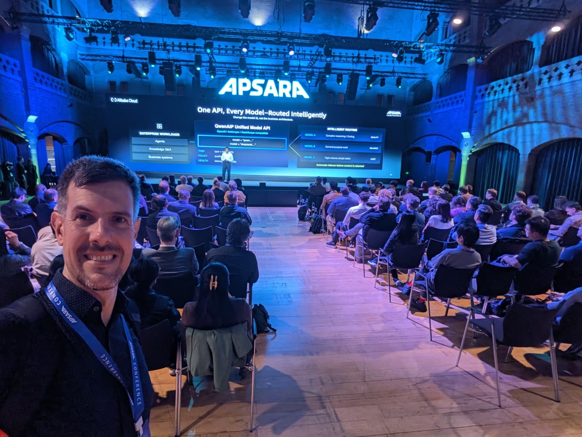 Luca Berton smiling in a selfie in the Beurs van Berlage, with rows of attendees and the blue-lit Apsara stage behind him