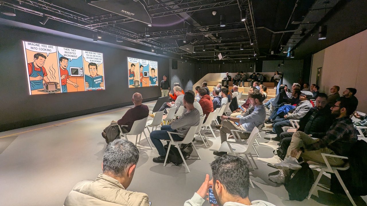 The room during the second talk, with a three-panel comic about cooking and microwave recipes on the screens and the speaker standing in front