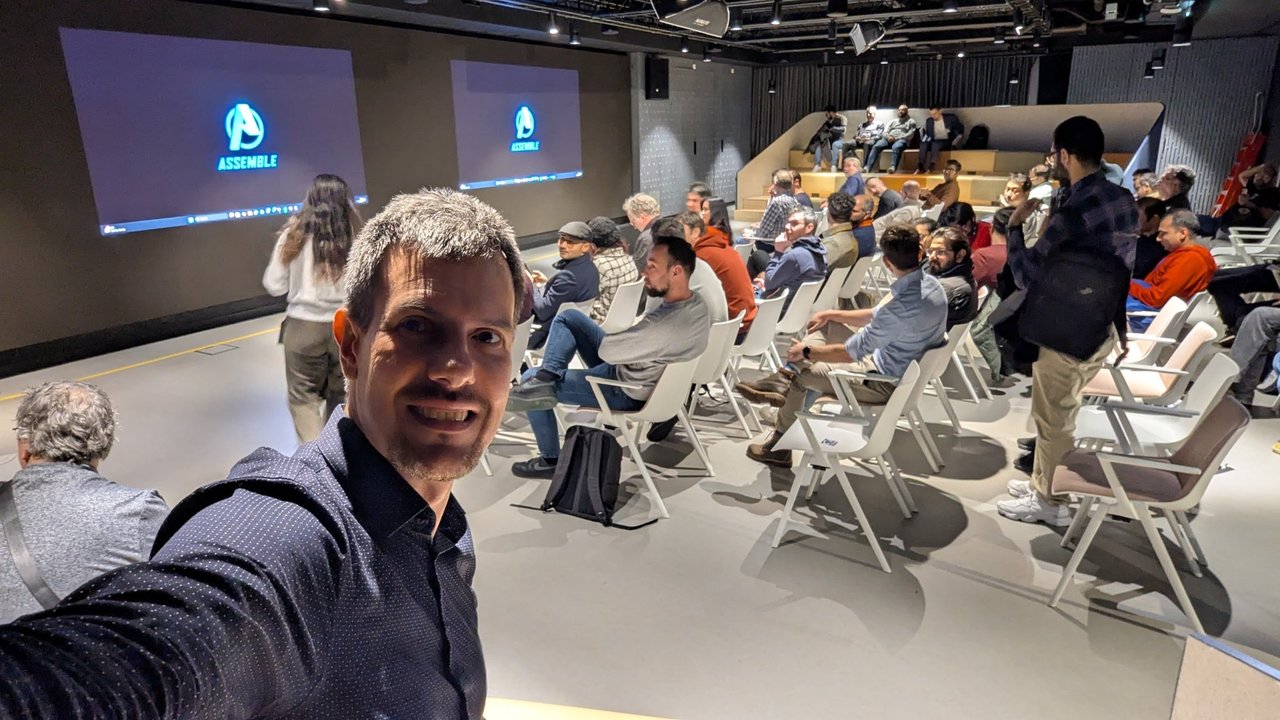 The meetup room before the start, with an Assemble title slide on the screens and people taking their seats