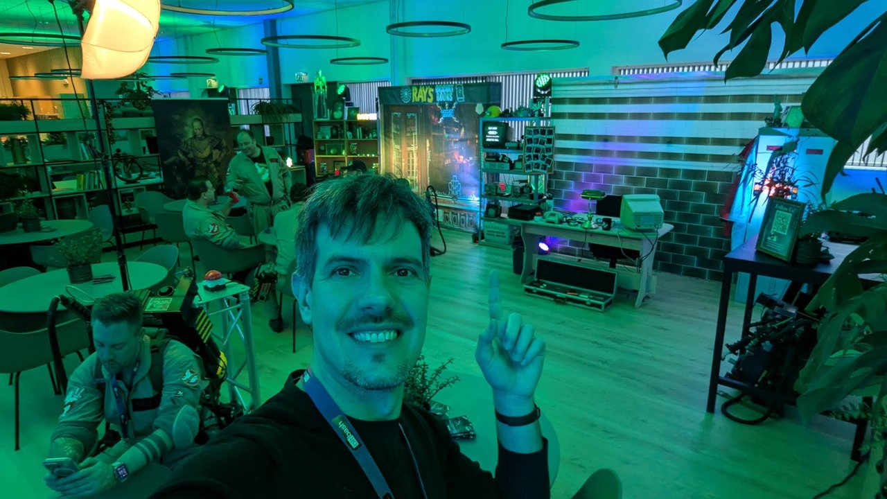 Luca Berton taking a selfie in the Ghostbusters-themed lounge at BitBash 2025, with a Ray's Occult Books set and people in Ghostbusters costumes behind him