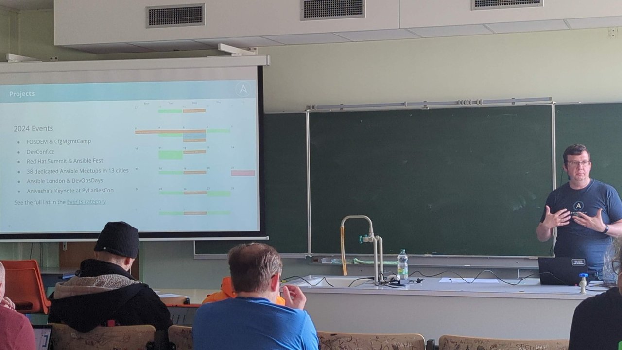 The State of the Ansible Community 2025 talk in a classroom at CfgMgmtCamp, with a slide listing 2024 events such as FOSDEM, CfgMgmtCamp, DevConf.cz and 38 dedicated Ansible meetups in 13 cities