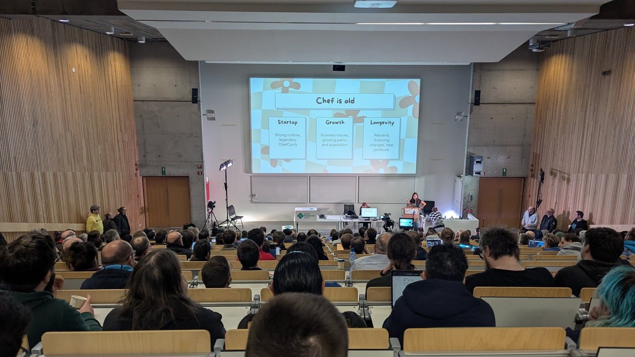 A slide titled Chef is old, with three boxes for startup, growth and longevity, in the full main lecture hall at CfgMgmtCamp 2025