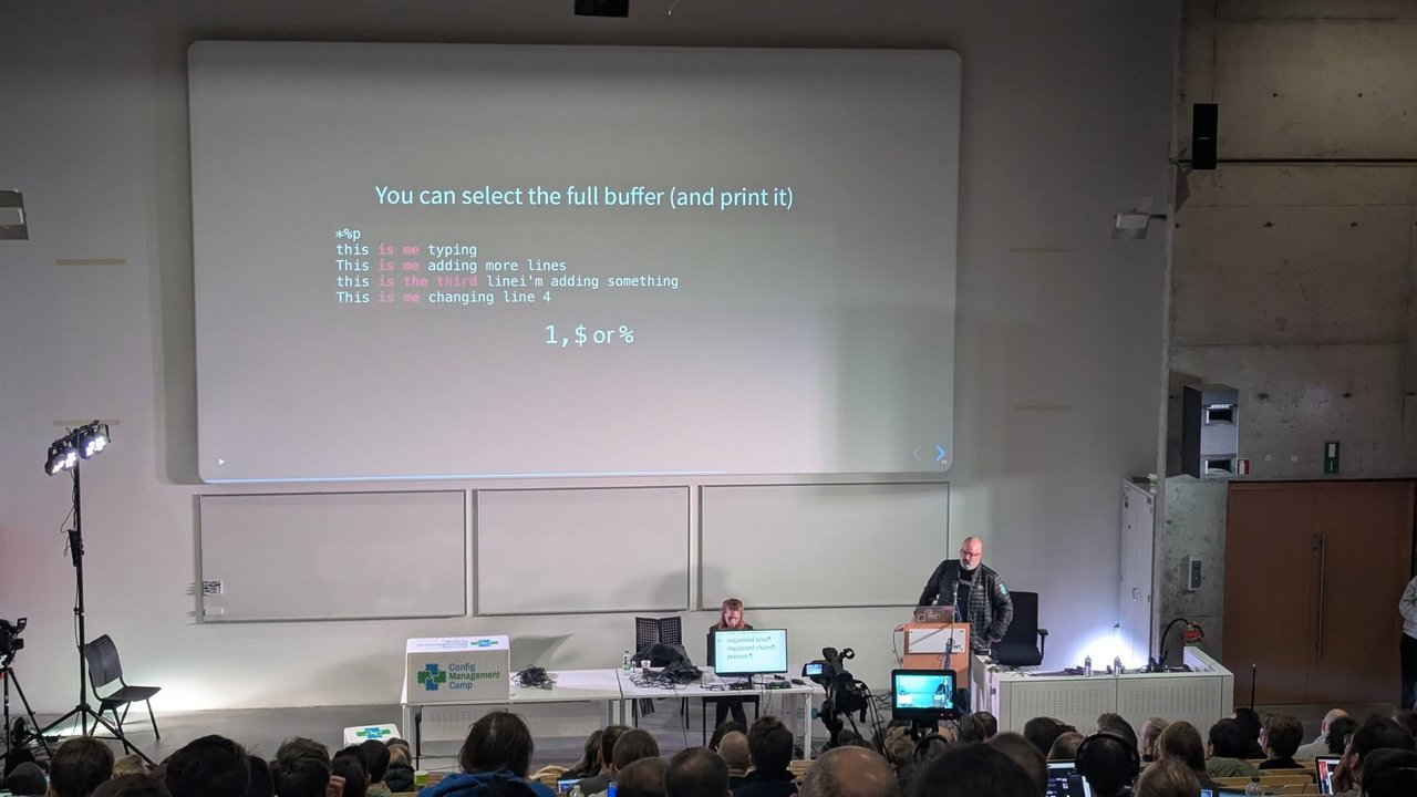 A slide titled You can select the full buffer and print it, showing ed commands, with the speaker at the lectern at CfgMgmtCamp 2025