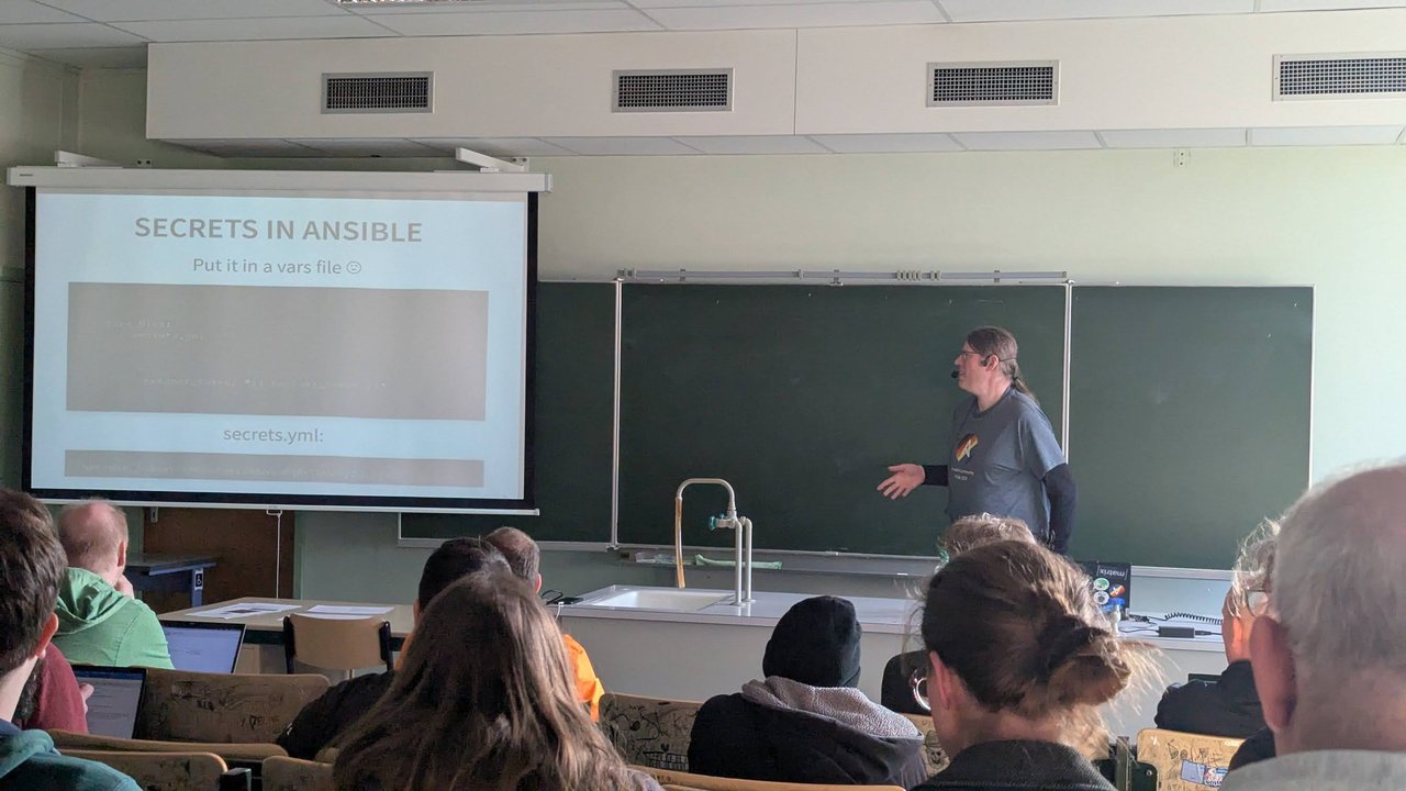 A speaker presenting Secrets in Ansible to a classroom audience at CfgMgmtCamp 2025 in Ghent