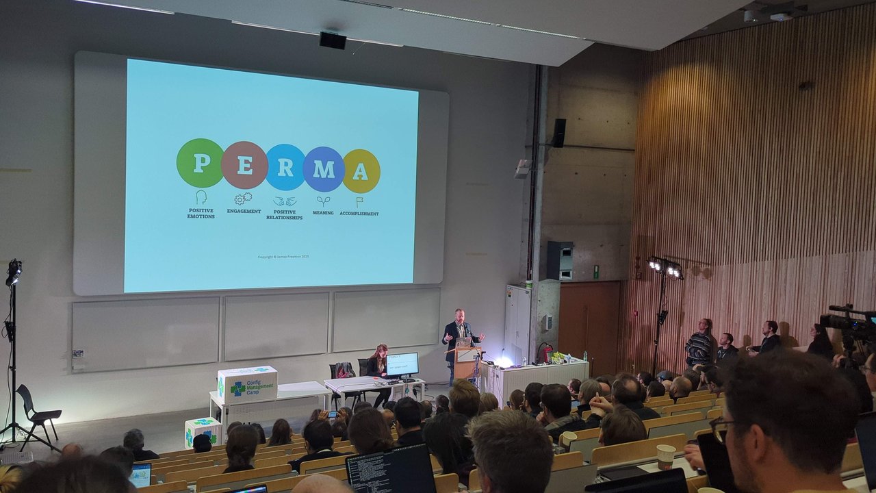 James Freeman presenting the PERMA model of positive psychology in the main auditorium at CfgMgmtCamp 2025