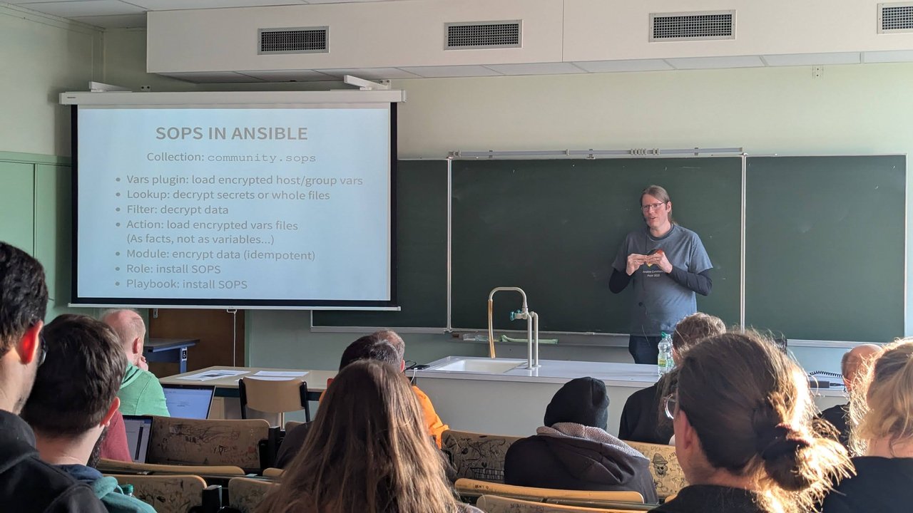 A speaker presenting the community.sops collection features in a classroom at CfgMgmtCamp 2025 in Ghent