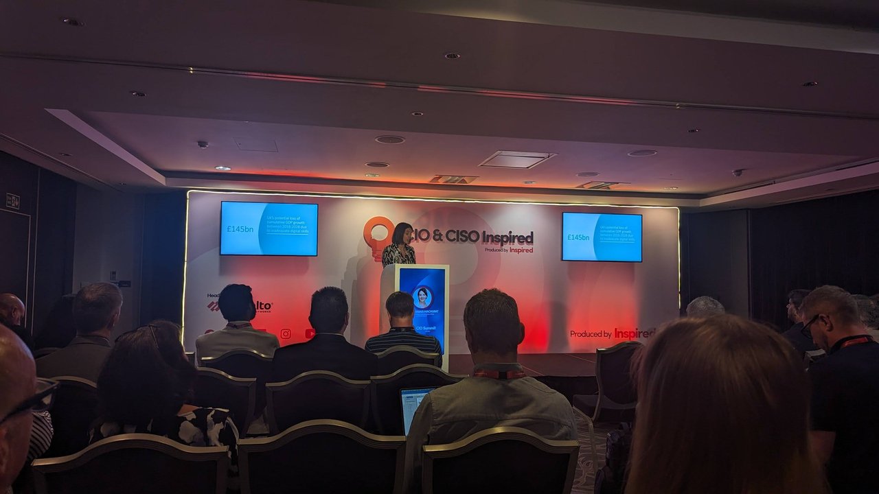 Speaker at the podium with the slide £145bn, UK's potential loss of cumulative GDP growth between 2018 and 2028 due to inadequate digital skills, on both screens