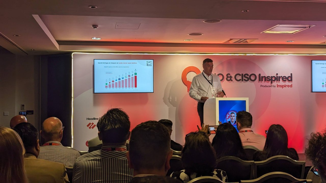 Speaker at the podium in front of the CIO & CISO Inspired backdrop, with a chart on the screen titled GenAI brings an impact at scale never seen before