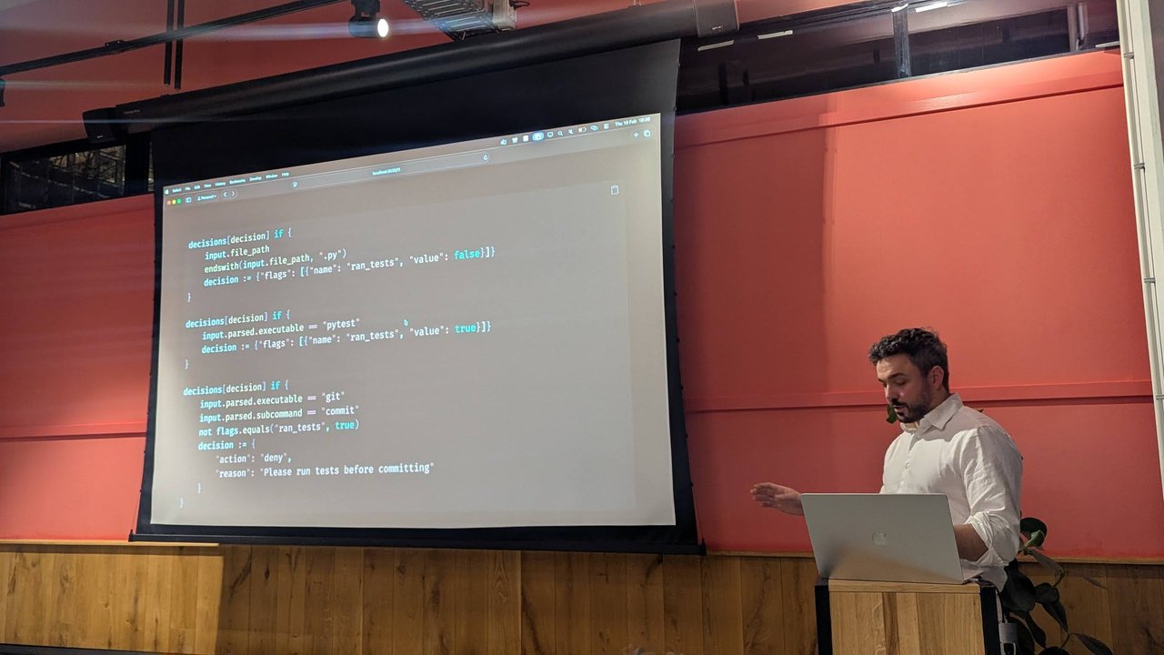 A slide at Claude Code Meetup Amsterdam with three rules: editing a .py file sets ran_tests to false, running pytest sets it to true, and git commit is denied with "Please run tests before committing" unless ran_tests is true