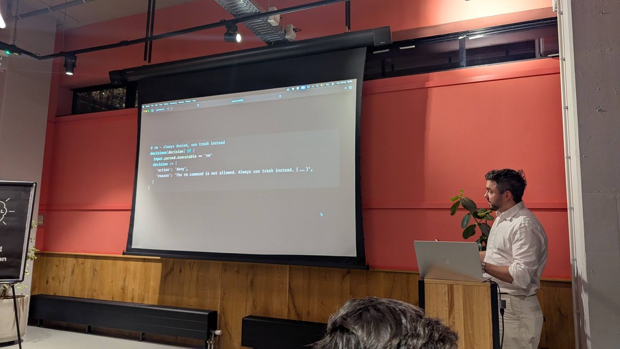 A slide at Claude Code Meetup Amsterdam with a Rego-style rule that denies any command whose parsed executable is rm, with the reason "The rm command is not allowed. Always use trash instead."
