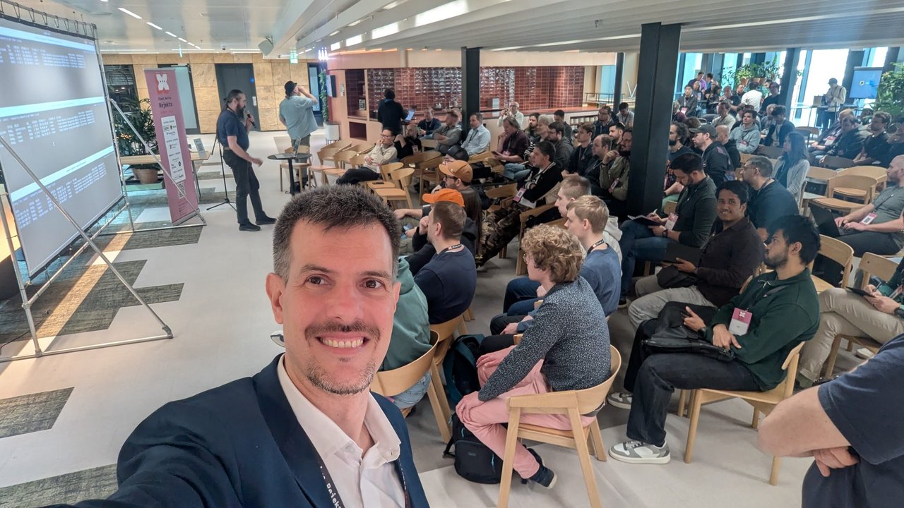 Luca Berton, Master of Ceremonies, in front of a packed room at Cloud Native Rejekts 2026 at Miro HQ in Amsterdam
