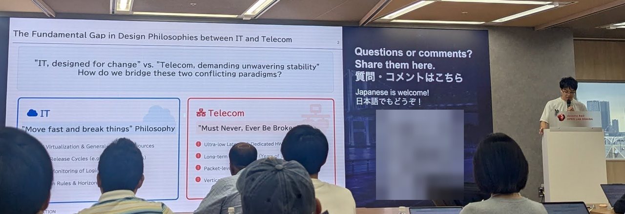 Slide: The Fundamental Gap in Design Philosophies between IT and Telecom, with the KDDI speaker at the lectern