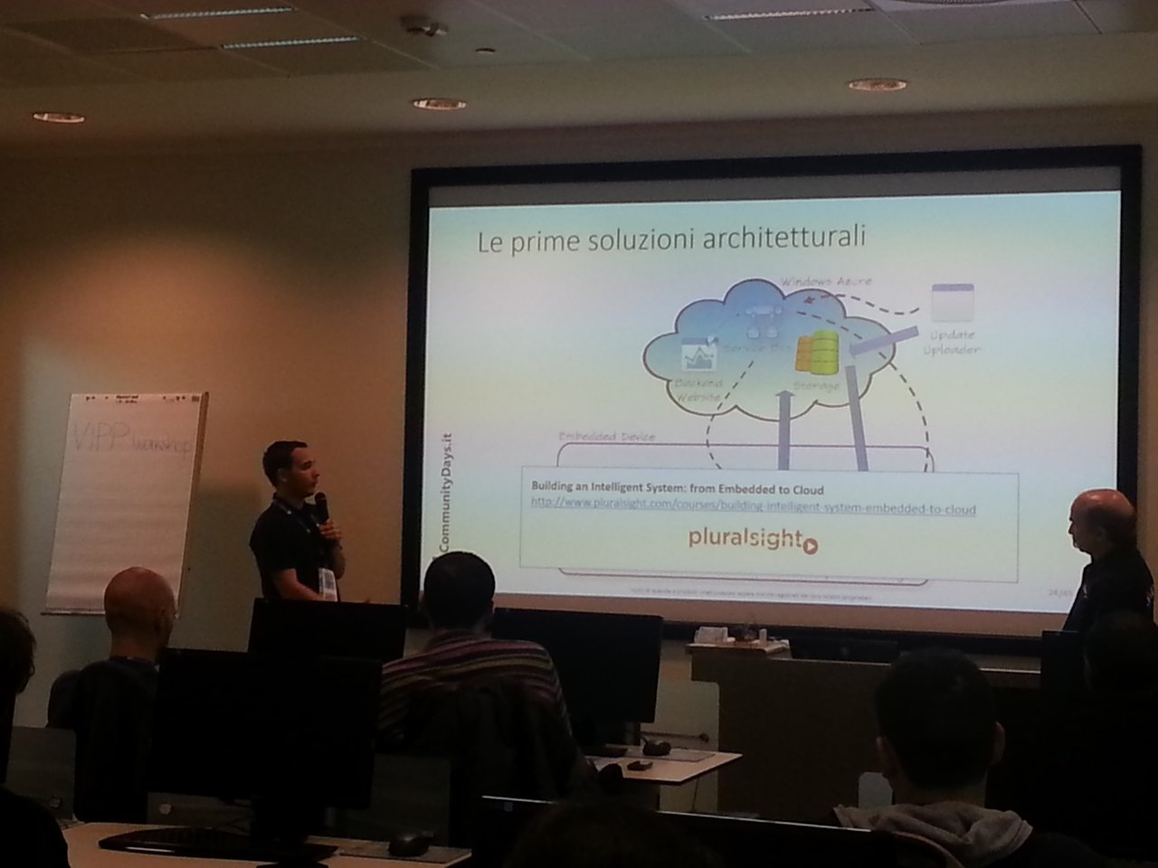 Two presenters in the IoT session at Community Days 2015 with a slide titled Le prime soluzioni architetturali: a Windows Azure cloud with backend website, Service Bus and storage, an update uploader and an embedded device