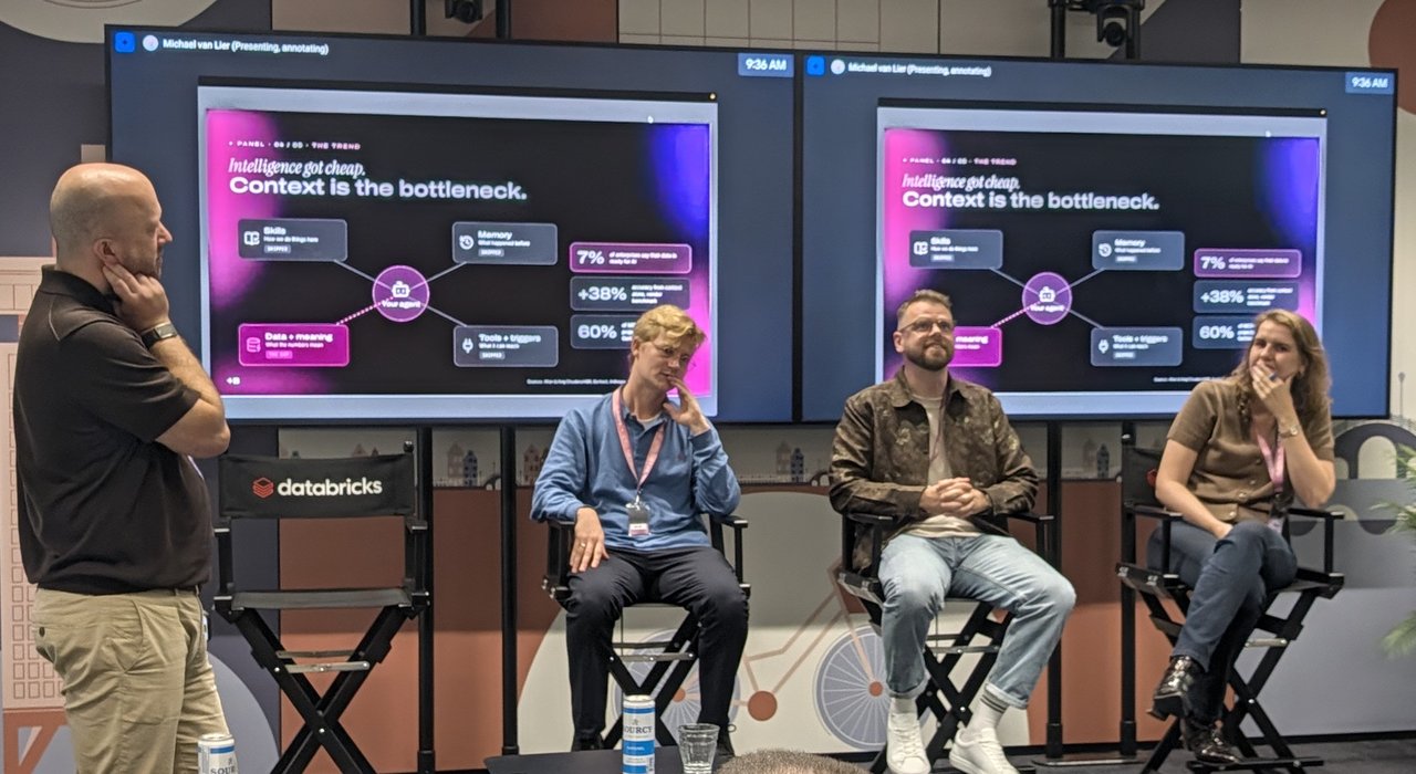 Moderator and three panellists on stage under two screens showing the slide Intelligence got cheap. Context is the bottleneck, with Skills, Memory, Tools and Data around Your agent