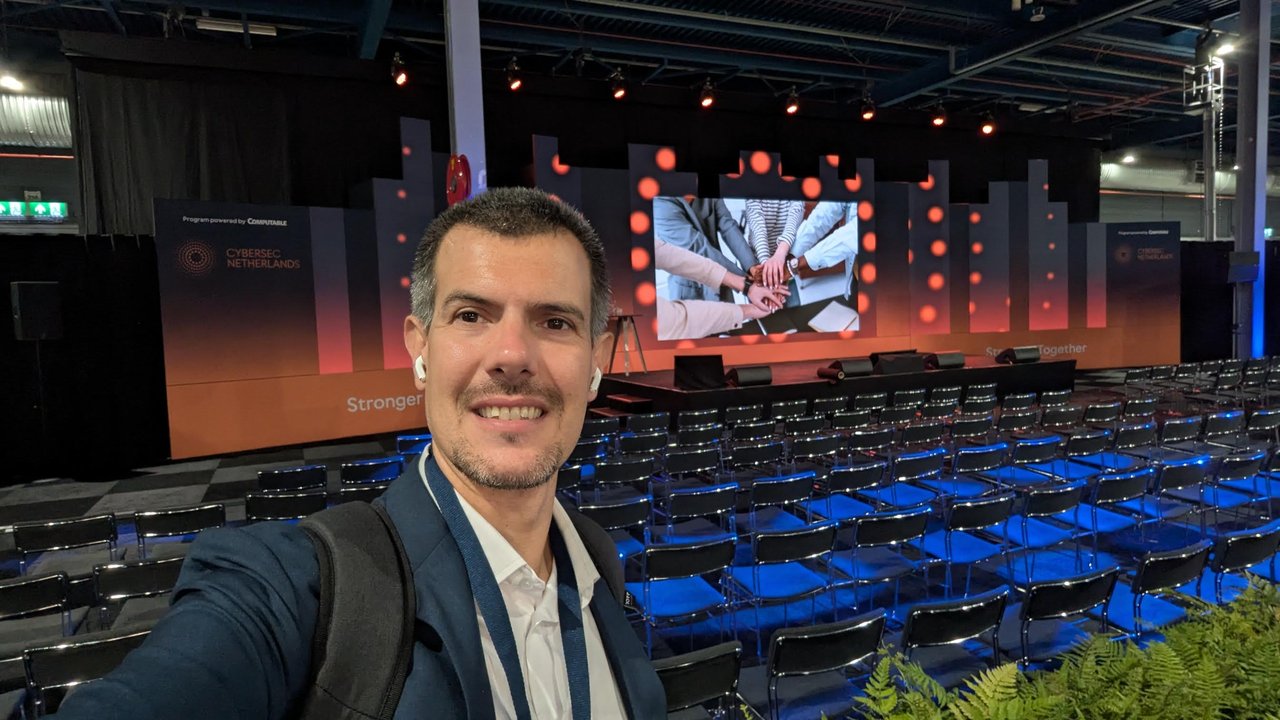 Luca Berton taking a selfie in front of the empty Cybersec Netherlands main stage, with rows of chairs, a Stronger Together banner and a Program powered by Computable panel