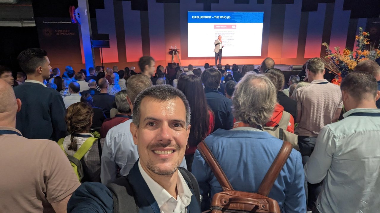 Luca Berton taking a selfie at the back of a packed main hall during a keynote, with the slide EU Blueprint - The Who (II) and a CSIRTs Network box on the screen
