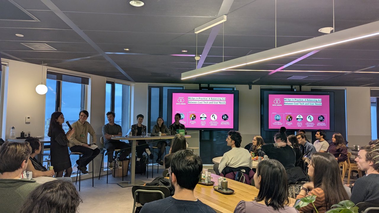 Data Union Amsterdam MLOps in Practice panel, with the moderator and four guest speakers seated in front of the pink title slide